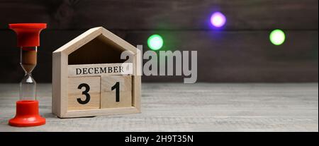 Christmas decorations on a wooden background: wooden cubes with the numbers December 31, red hourglass. Selective focus. Banner Stock Photo