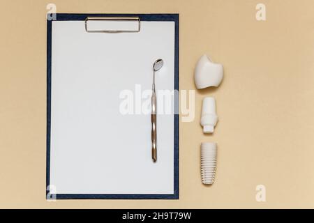Dental implant and folder with clip for paper sheets A4 on beige background. Dental implant model of artificial tooth. Concept of dentistry and medica Stock Photo