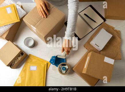 A warehouse worker packs a cardboard box with a tape dispenser. Stock Photo