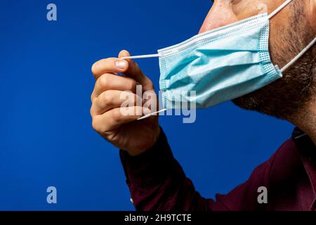 Detail of face of hispanic man taking off his surgical mask isolated on blue background, he gets rid of the mask astied from the desperate situation Stock Photo