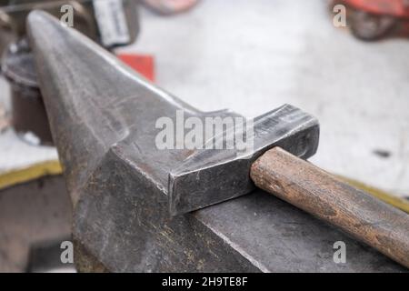 Vintage iron hammer with rustic wooden handle lies on large metal anvil in brightly lit farriery workshop extreme close view Stock Photo