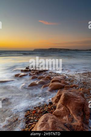 sunset over the sea and rocks at compton bay on the coastline of the isle of wight, shoreline of the isle of wight at compton bay at sun down, moody. Stock Photo