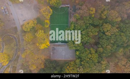 Football field with green grass and basketball court in city park in autumn. Leaf fall in the park. Aerial view. Stock Photo