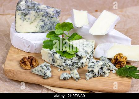 Many different varieties of cheese: blue, brie, camembert and other with walnuts on wooden board background. Stock Photo