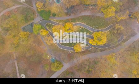 Bicycle path imitating a mountain serpentine track in the city park in autumn. Leaf fall in the park. Aerial view. Stock Photo