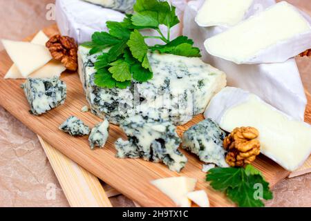 Many different varieties of cheese: blue, brie, camembert and other with walnuts on wooden board background. Stock Photo