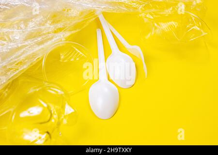 Plastic spoons, forks, bottles and cups as a disposable waste on bright yellow background. Environmental pollution and litter recycling concept. Stock Photo