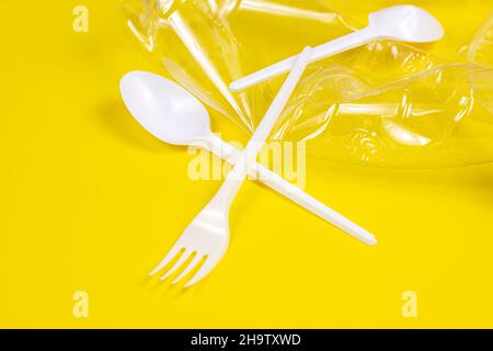 Plastic spoons, forks, bottles and cups as a disposable waste on bright yellow background. Environmental pollution and litter recycling concept. Stock Photo
