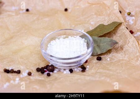 White sea salt in glass bowl with spices on light beige parchment paper textured background. Stock Photo
