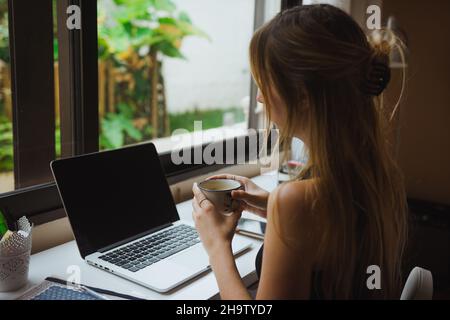 Girl holding a cup of coffee, working online Stock Photo