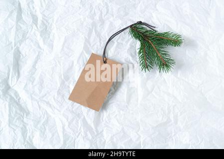 Close up of green fir branch with blank white label. Price tag mockup scene on tissue paper background. Christmas composition, top view, flat lay Stock Photo