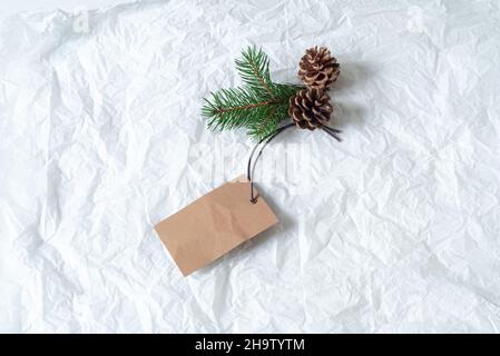 Close up of green fir branch and pine cones with blank white label. Price tag mockup scene on tissue paper background. Christmas composition, top view Stock Photo