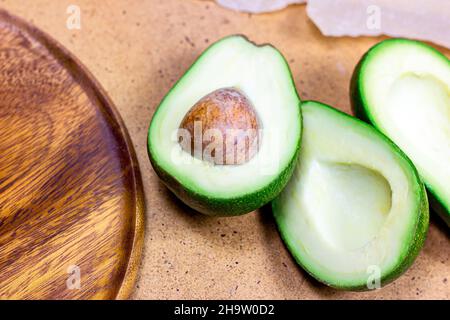 Fresh half sliced green avocado pieces ready to eat on brown wooden board background. Stock Photo
