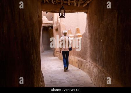 A lonely Western female tourist walking in the narrow street in Ushaiqer Heritage Village, Saudi Arabia. Back view. Stock Photo