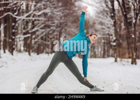 Sportswoman in warm outfit doing yoga exercises in snowy forrest. Fitness outdoors, snow, cold, winter yoga Stock Photo