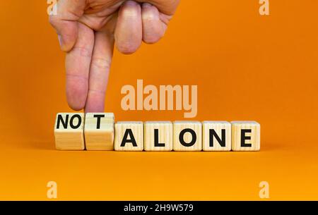 You are not alone symbol. Businessman turns wooden cubes and changes words alone to not alone. Beautiful orange table orange background, copy space. B Stock Photo