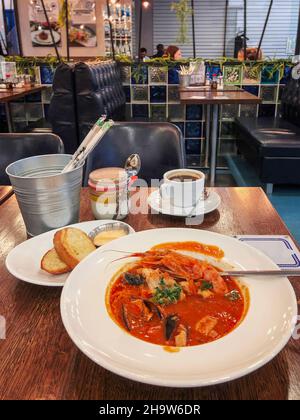 Tomato gazpacho soup with seafood, bread garlic toasts and cup of coffee standing on table in fish restaurant, selectve focus Stock Photo