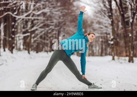 Sportswoman in warm outfit doing yoga exercises in snowy forrest. Fitness outdoors, snow, cold, winter yoga Stock Photo
