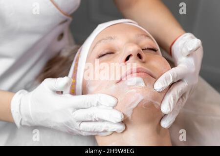Close-up beautician doctor hand making anti-age procedure, mask and peeling for young attractive female client at beauty clinic. Cosmetologist Stock Photo