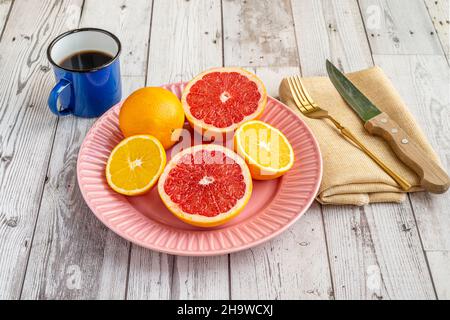 Plate of halved citrus fruits, oranges and grapefruits with coffee and cutlery on light wooden table Stock Photo