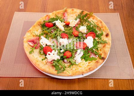 Pizza with burrata cheese, cherry tomatoes, arugula and serrano ham cooked in a stone oven Stock Photo