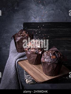 Vertical closeup shot of three delicious chocolate muffins on a dark gray background Stock Photo