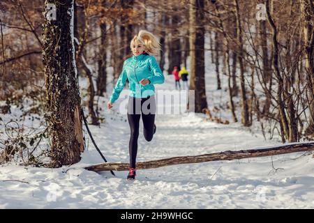 Sportswoman running in woods at snowy winter day. Outdoor sport, cardio exercises, winter fitness Stock Photo