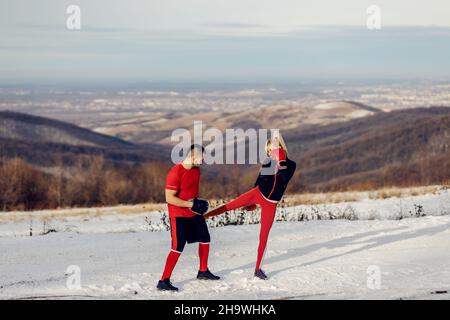 Sportswoman sparring and kicking pad in nature at snowy winter day with her coach. Boxing, winter fitness, outdoor fitness Stock Photo