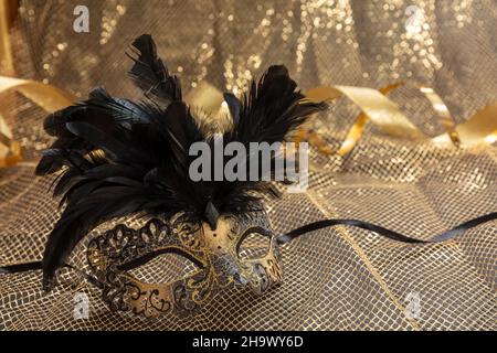 Carnival Venetian mask with black feathers on golden color sparkling background. Traditional festival female disguise, Mardi Gras event masquerade Stock Photo