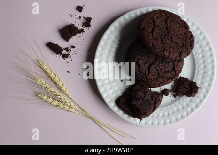 a top view of a grey ceramic plate with traditional American chocolate chip cookies and three ears of corn. lilac background Stock Photo