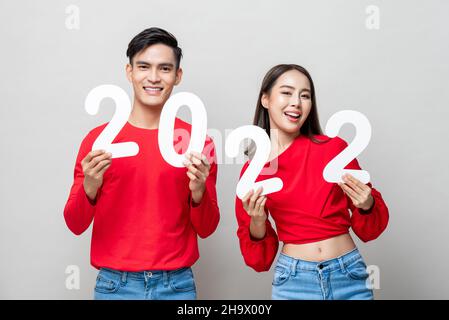 Young smiling Asian couple showing number 2022 in isolated light gray background for new year concept Stock Photo