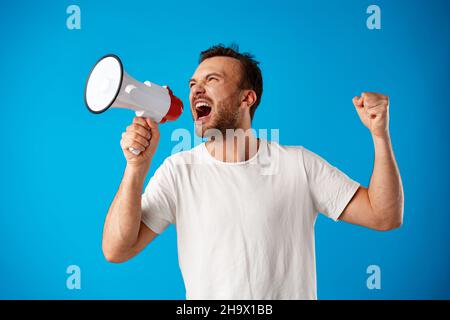Handsome man over blue wall shouting through a megaphone. Stock Photo