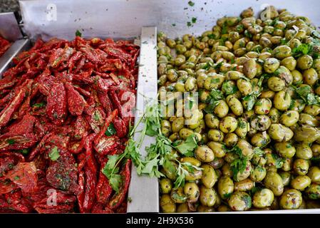 Close up of dried tomatoes and green olives with fresh herbs at market stall in Sicily, Italy. Stock Photo