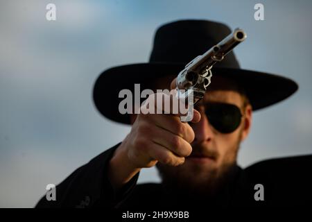 Cowboy shooter in black suit and cowboy hat. Serious man with wild west guns, retro pistol revolver and marshal ammunition. American western Sheriff Stock Photo