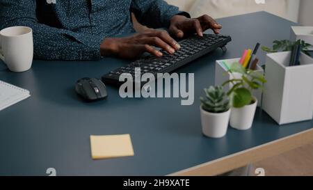 Top view of black man african american hands typing on computer keybord on a blue desk. Remote worker using PC, working from home, browsing searching online web internet communication Stock Photo