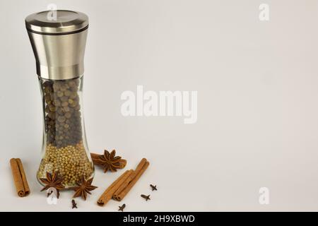 Pepper mill with different types of peppers in layers, as well as stars of anise and cinnamon on a white background. On the right is a place for an in Stock Photo