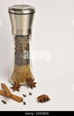Pepper mill with different types of peppers in layers, as well as stars of anise and cinnamon on a white background. On the right is a place for an in Stock Photo