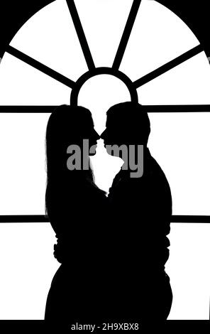 Black and white illustration of figures of a guy and a girl hugging against the background of a stained glass window Stock Photo