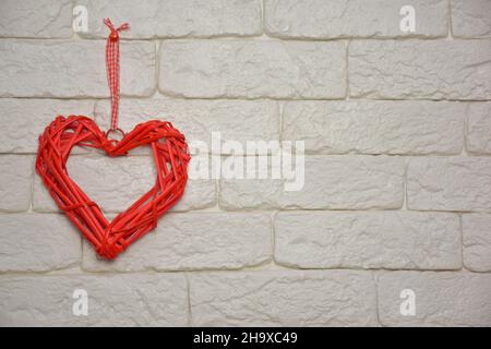 Stylized red heart made of woven natural material on the left against a light brick wall. On the right is a place for an inscription or congratulation Stock Photo
