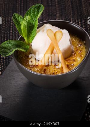 sweet dessert creme brulee with scoop of ice cream, served in a small ceramic bowl on a stone plate, vertical photo on dark background Stock Photo