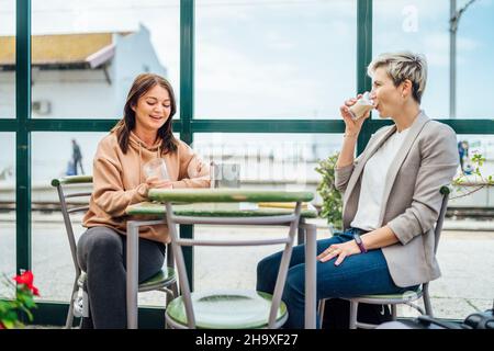 Two travelling women with luggage drinking coffee at train station, Portugal Stock Photo