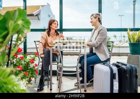 Two travelling women with luggage drinking coffee at train station, Portugal Stock Photo