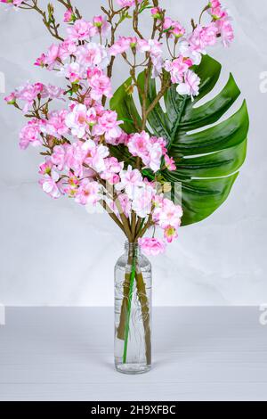 A bouquet of spring flowers in a vase, pink cherry blossom in a glass bottle on a gray table. Home interior decor. Floral still life, postcard, beauti Stock Photo