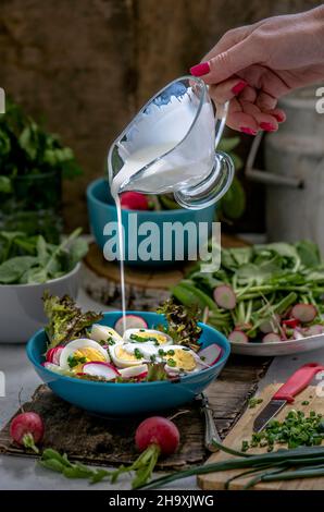 Dressing being poured over a salad with radishes and boiled eggs Stock Photo