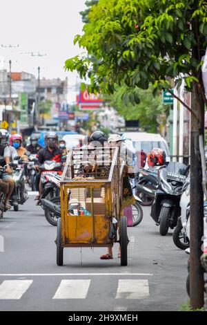 A hardworker scavenger pulling his cart in a cloudy morning after rain, on asphalt road. Solo - Indonesia. December 9, 2021 Stock Photo