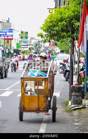 A hardworker scavenger pulling his cart in a cloudy morning after rain, on asphalt road. Solo - Indonesia. December 9, 2021 Stock Photo