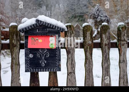christmas card in bright red envelope sticking out of snow covered letterbox mounted on garden gate of house zala county hungary Stock Photo
