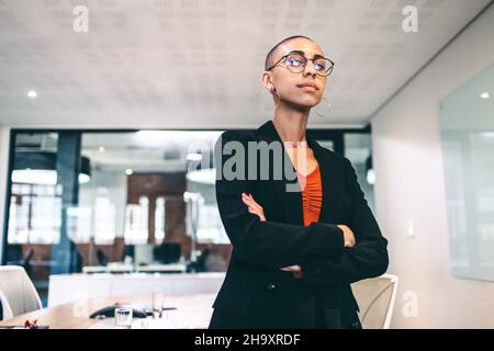 Self-assured businesswoman standing with her arms crossed. Confident young businesswoman looking at the camera in a boardroom. Young businesswoman wea Stock Photo