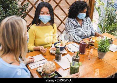 Happy multiracial young friends eating at brunch restaurant during coronavirus outbreak - Focus on asian girl face Stock Photo