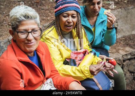 Multiracial women having fun eating together after trekking day in to the wood - Focus on african female face Stock Photo